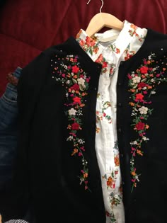 a black sweater with colorful flowers on it and a white shirt underneath the jacket is hanging on a hanger