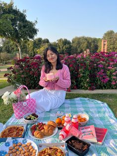 a woman sitting on the ground with many plates of food and drinks in front of her