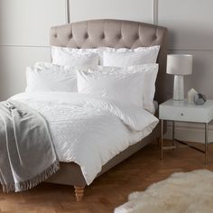 a bed with white comforter and pillows in a room next to a night stand