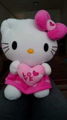 a hello kitty stuffed animal with a heart on it's chest sitting in someones lap