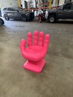 a pink hand shaped object sitting on top of a cement floor next to parked cars