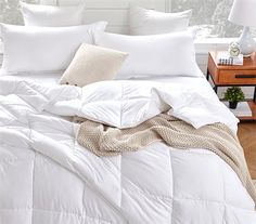 a bed with white comforters and pillows on top of it in front of a window