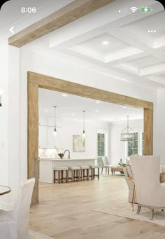 an open concept living and dining room with wood flooring, white walls and wooden beams