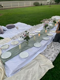 a long table with plates and candles on it in the middle of a grassy field