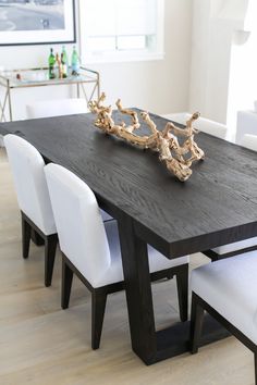 a dining room table with white chairs and a large wooden branch on the center piece