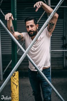 a man with tattoos on his arms leaning against a metal fence and looking at the camera