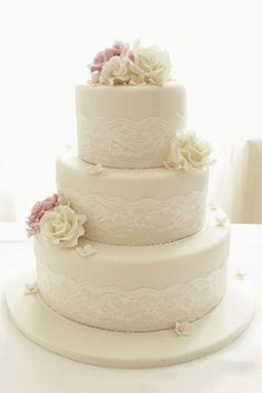 a three tiered wedding cake with white lace and pink flowers on the bottom layer