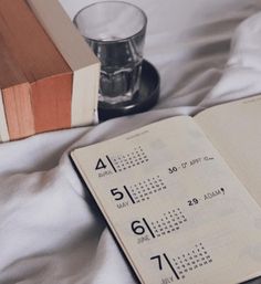 an open book sitting on top of a bed next to a glass filled with water