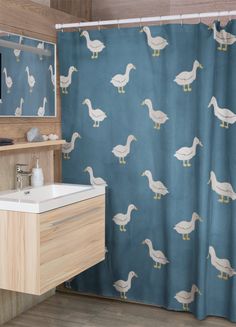 a bathroom with a blue shower curtain and white ducks on the wall next to it