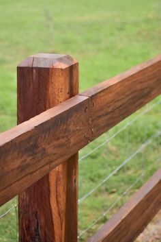 a bird perched on the top of a wooden fence in front of a grassy field