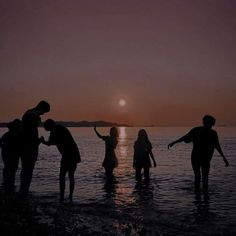 four people standing in the water at sunset with their arms up and one person holding his hand out