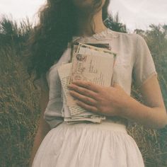 a woman is standing in the grass holding some papers and looking up at her face