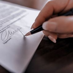 a person writing on a piece of paper with a pen in their left hand and the other hand holding a pencil