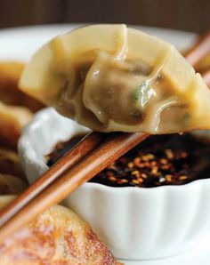 chopsticks are holding dumplings with sauce in the bowl and on top of them