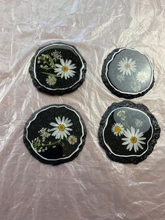 three black plates with white daisies on them sitting on a plastic tablecloth covered surface