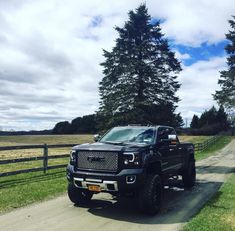 a black truck parked on the side of a dirt road next to a wooden fence