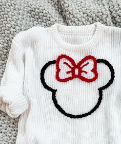 a white sweater with a red bow on the front and black ears on the back