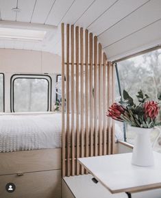 the interior of a camper with a bed, desk and flower vase on it