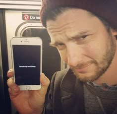 a man holding up his cell phone in front of the camera while standing next to a subway car