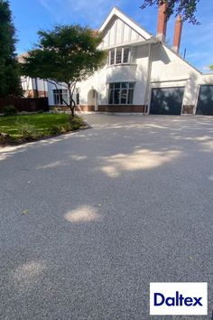 an empty driveway in front of a large white house with garage doors and trees on both sides