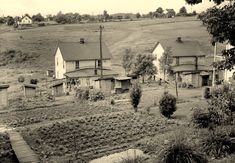 an old black and white photo of some houses in the country side, with a path leading up to them