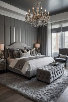 a bedroom with a large bed, chandelier and two chairs in front of the window