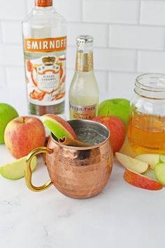 a copper mug filled with apple cider next to some apples and an apple slice