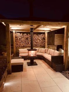 an outdoor living area with couches and firewood stacked on the wall at night