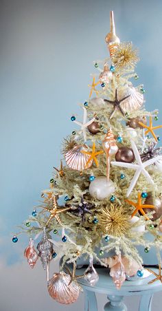 a white christmas tree decorated with seashells and starfish on a blue table