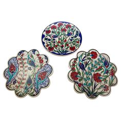 three decorative plates with flowers and birds painted on the front, one in red, one in blue