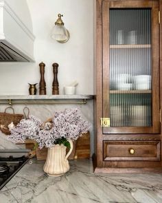 a vase filled with purple flowers sitting on top of a counter next to a stove