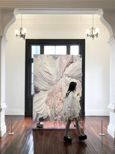 a woman walking in front of a large painting