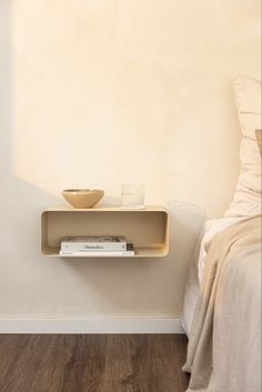 a small shelf on the wall next to a bed with a bowl and glass in it