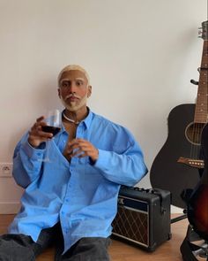 a man sitting on the floor with a glass of wine in his hand and guitar behind him