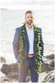 a man in a blue suit with a lei around his neck standing on the beach