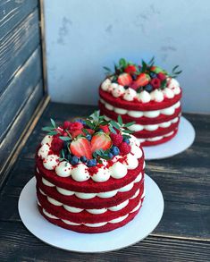 two red velvet cakes with berries and whipped cream frosting on top are sitting on white plates