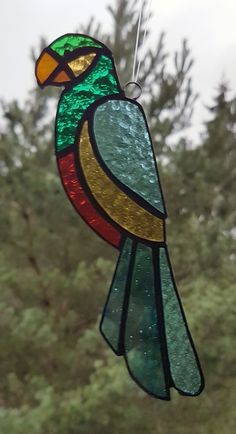 a stained glass bird hanging from the side of a window with trees in the background