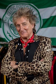 a man with his arms crossed standing in front of a green and white striped flag