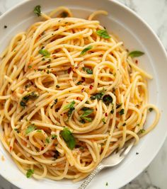 a white bowl filled with pasta and garnished with parsley on the side