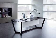 an office desk with a laptop on it in front of large windows and bookshelves