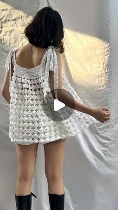 a woman in white crocheted dress and black booties standing up against a white backdrop