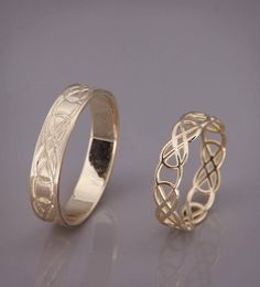 two gold wedding rings with intricate designs on each side, set against a gray background