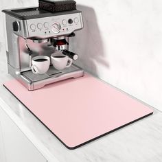 a pink placemat with two coffee cups on it next to an espresso machine