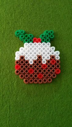 a piece of art made out of legos on green carpeted area with red, white and green beads