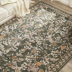 a green rug with flowers and leaves on the floor in a living room next to a white couch