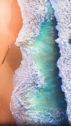 an aerial view of the ocean and beach with waves coming in from the shore, as seen from above