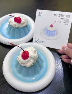 two desserts with cherries and whipped cream on them are displayed in front of a card