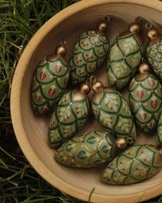 a wooden bowl filled with christmas ornaments on top of green grass covered ground next to trees