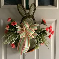 a door hanger decorated with flowers, grass and a bunny shaped basket hanging on the front door