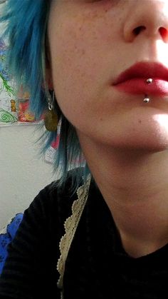 a woman with blue hair and piercings on her nose is looking at the camera